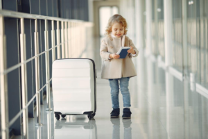 A happy little girl holding a suitcase and passport, excited about her international journey at the airport.