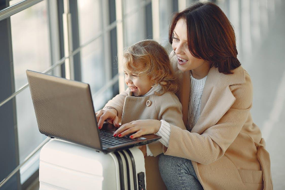 A delighted mother and daughter typing on a laptop in the airport, preparing for their journey.